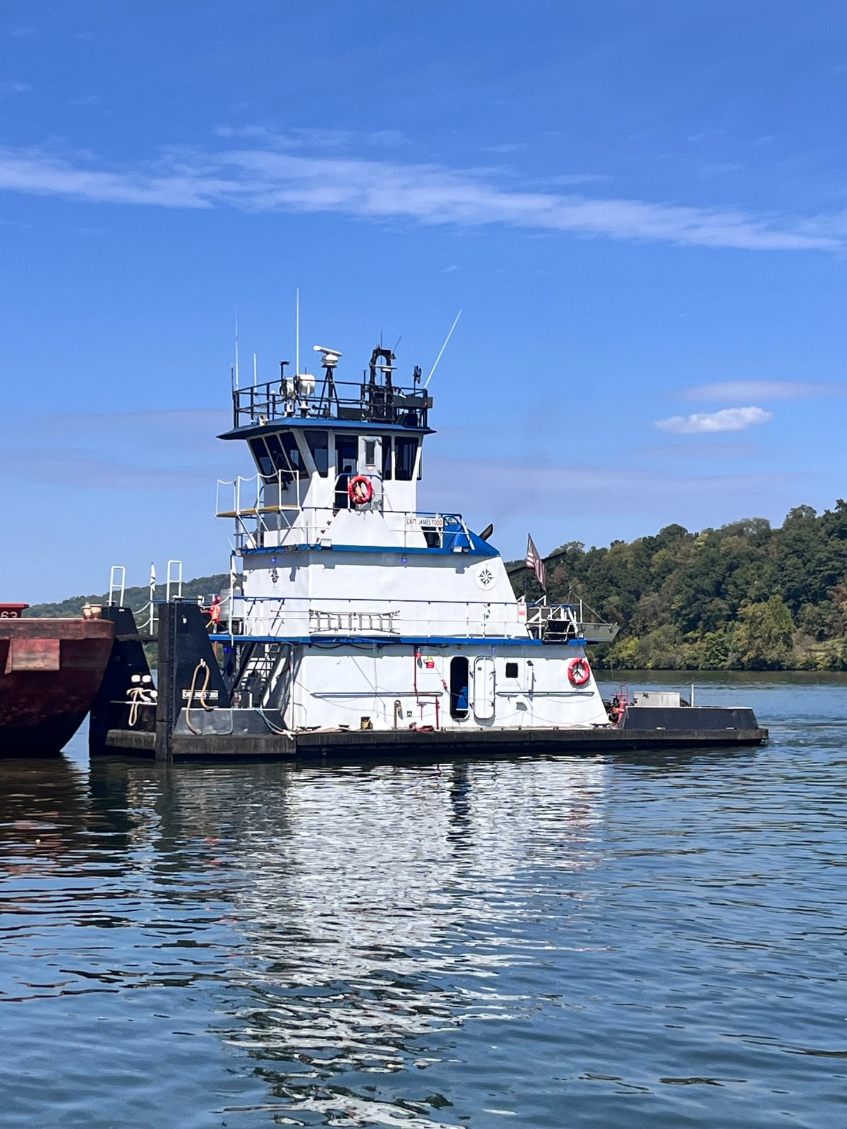 Capt. James Todd moored beside a barge on a sunny day, with its tall pilothouse above the white and blue decks.